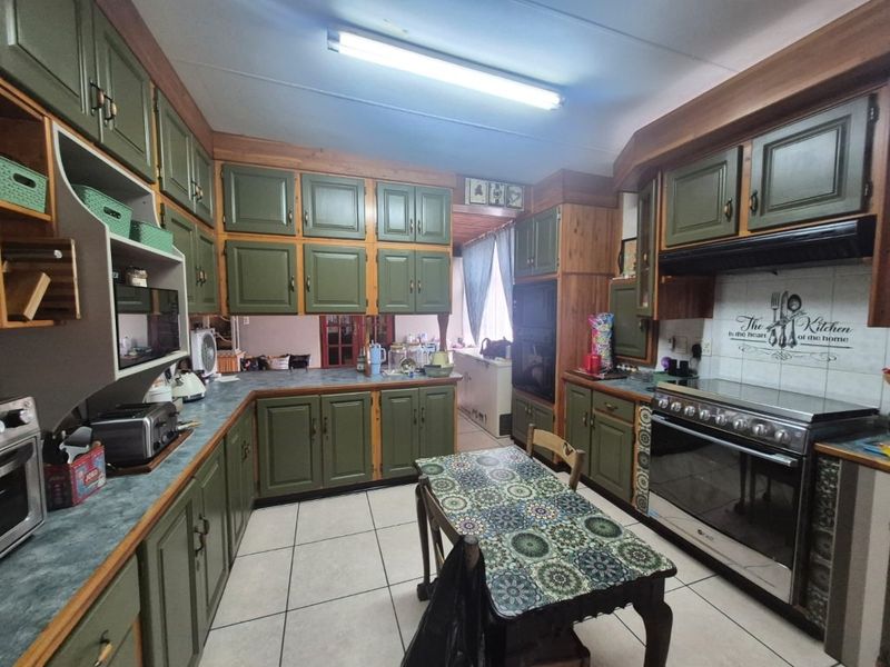 A dated kitchen featuring olive green cabinetry, laminate countertops, tiled flooring, and a built-in oven and hob setup.