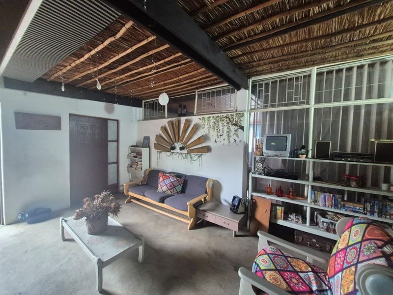 Living room featuring an exposed thatch ceiling with steel beam support, large windows, and concrete flooring, offering a rustic aesthetic with potential for modernization.