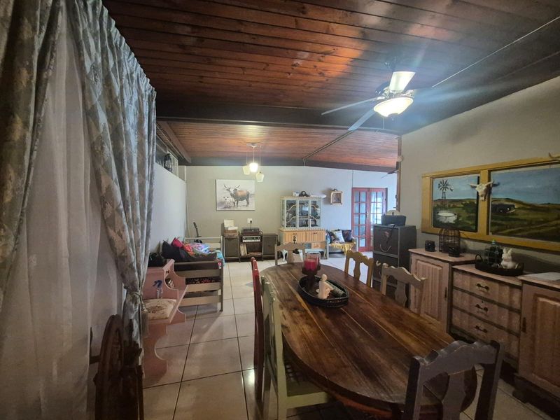 Spacious open-plan living and dining area featuring a high exposed timber ceiling, ceramic tiled flooring, and a ceiling fan.