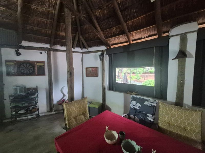 A rustic covered patio area featuring a traditional thatched roof with exposed timber beams and roller blinds, offering a cozy outdoor living space.
