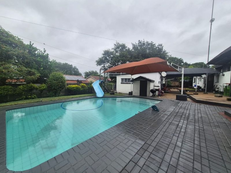 Outdoor pool area featuring a swimming pool with a slide, paved surround, and a shade sail covering a patio space.