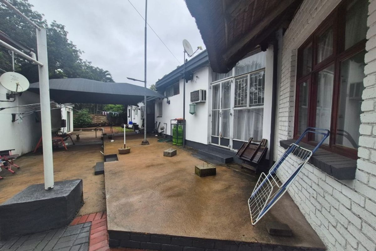 Rear exterior view of the house featuring a concrete patio area, thatched roof section, and brick wall construction.
