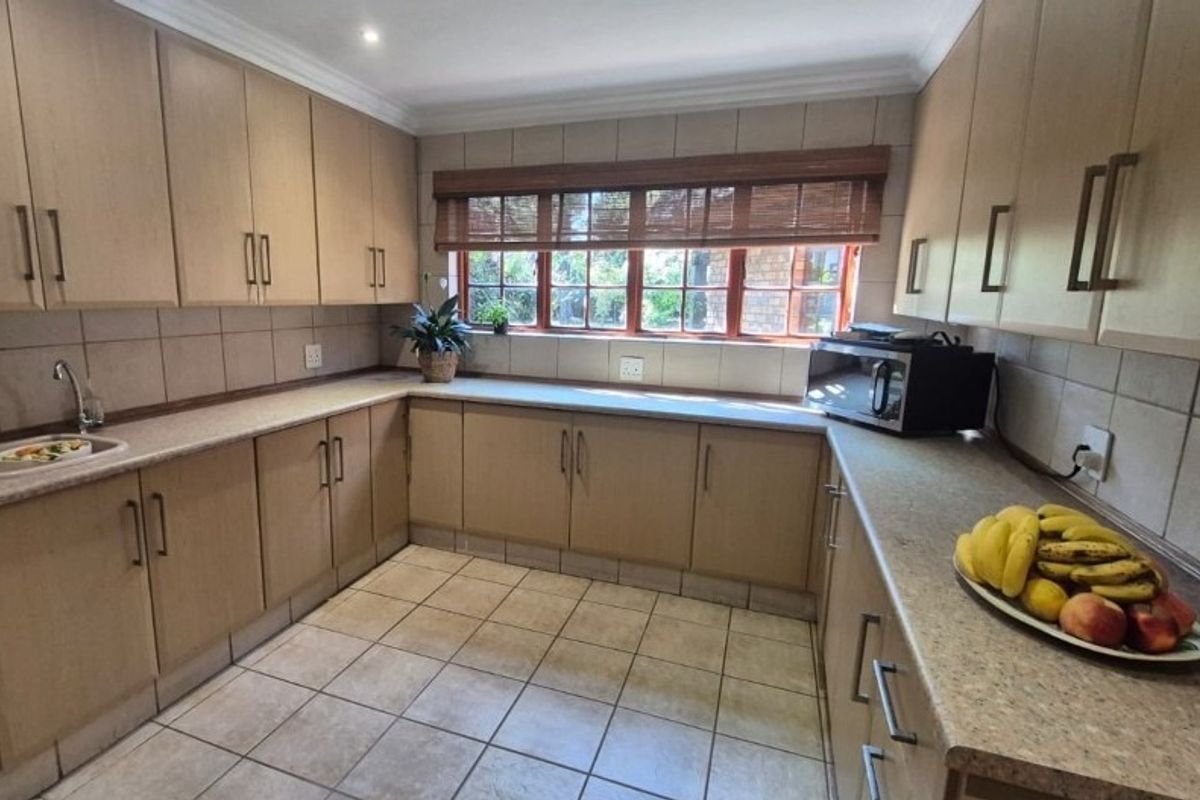 A functional kitchen featuring light wood-tone cabinetry, ample laminate counter space, ceramic tile flooring, and a large window providing natural light.