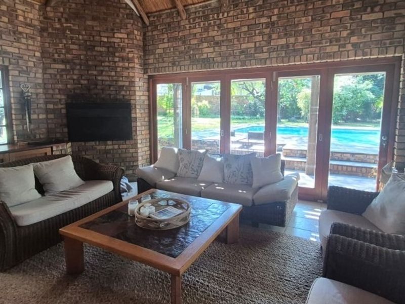 Spacious living room featuring exposed brick walls, a high thatched ceiling, and large bi-fold doors opening onto a pool area.