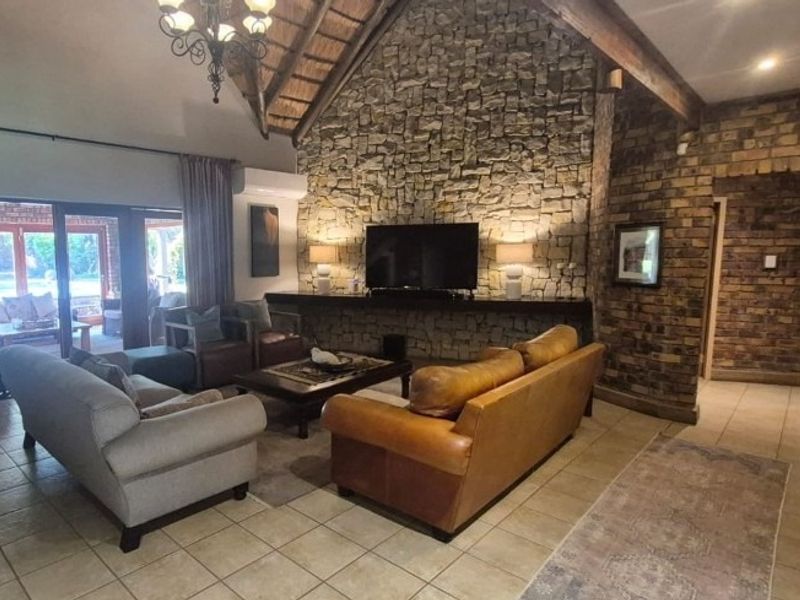 Spacious living room featuring a striking stone fireplace wall, exposed timber beams, high thatched ceilings, and large sliding doors leading to the patio.