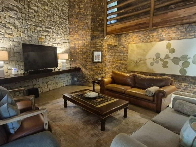Spacious living room featuring a striking stone feature wall, exposed brickwork, and a high-level timber mezzanine railing, creating a warm and textured atmosphere.