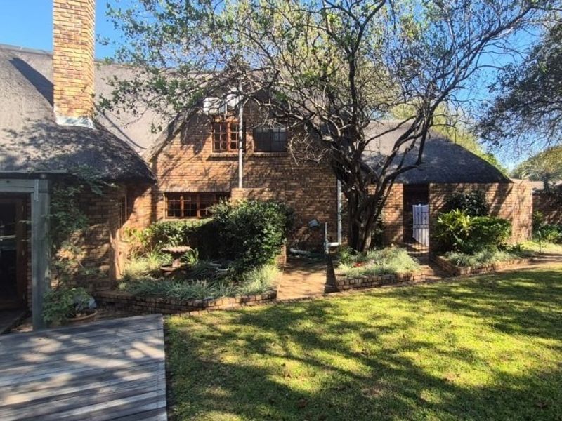 Rear view of a facebrick house featuring a traditional thatch roof, timber-framed windows, a brick chimney, and a wooden deck overlooking the garden.