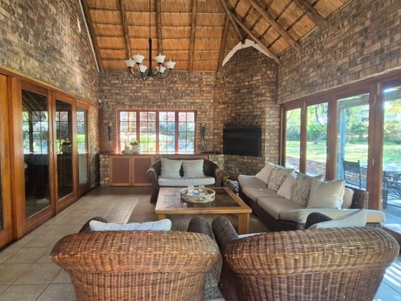 Spacious living room featuring exposed brick walls, a high thatched ceiling, and large timber-framed sliding doors providing ample natural light and garden access.