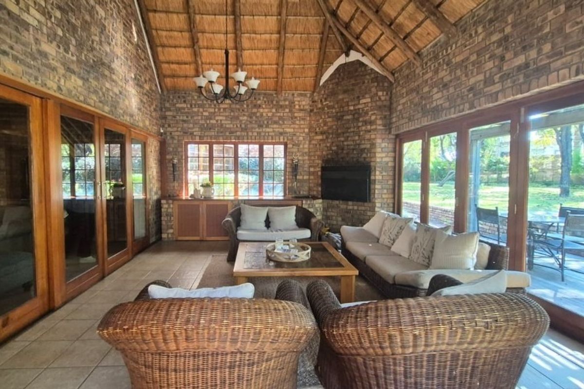 Spacious living room featuring exposed brick walls, a high thatched ceiling, and large timber-framed sliding doors providing ample natural light and garden access.