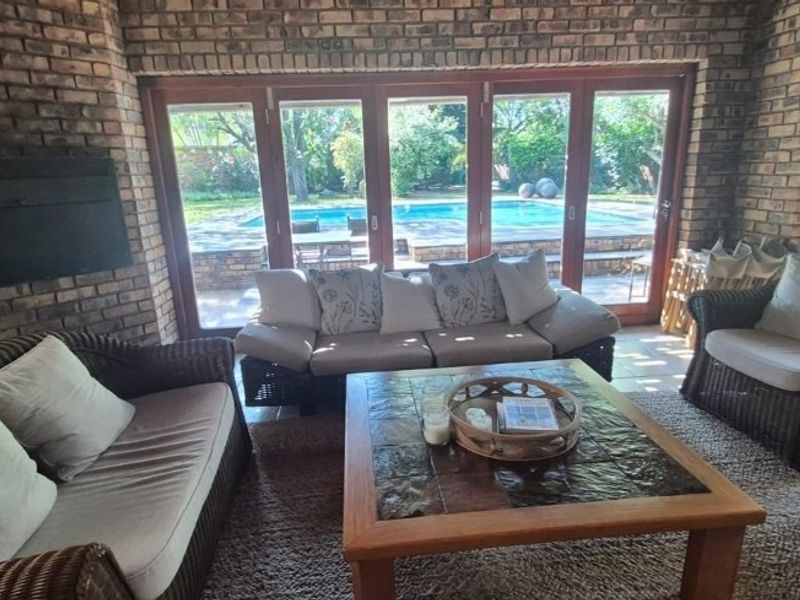 A covered patio area featuring exposed brick walls, a built-in fireplace, and large bi-fold doors opening onto a swimming pool and garden.