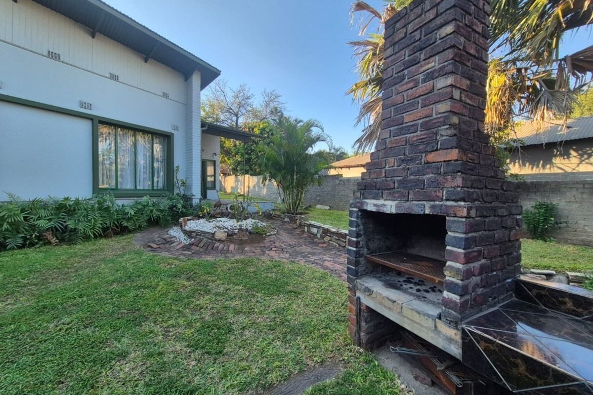 Rear garden area featuring a built-in brick fireplace, paved pathways, and established landscaping adjacent to the main house structure.