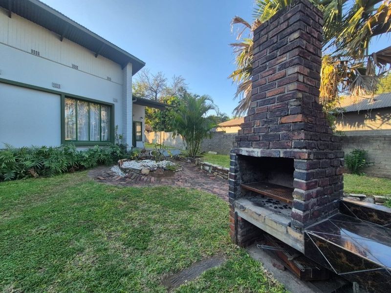 Rear garden area featuring a built-in brick fireplace, paved pathways, and established landscaping adjacent to the main house structure.