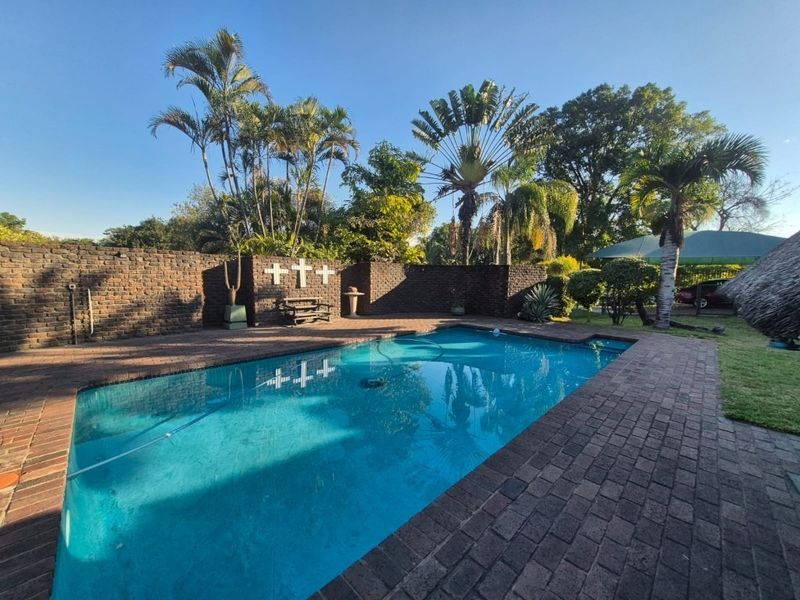 Outdoor swimming pool area featuring brick paving and a surrounding brick boundary wall, set within a landscaped garden environment.