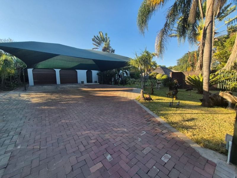 Front exterior view featuring a paved driveway, a large shade sail carport covering a double garage, and a well-maintained garden area.