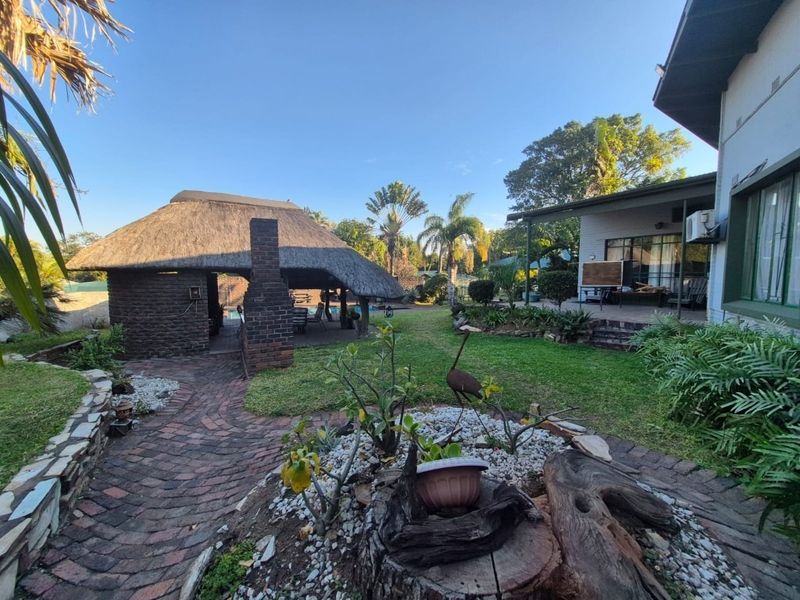 Spacious rear garden featuring a thatched lapa with a built-in brick braai, paved walkways, and a covered patio area.