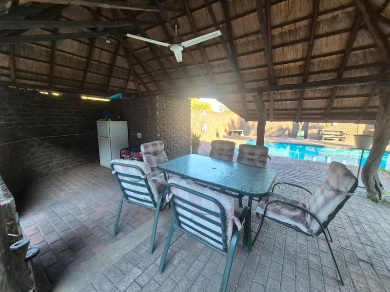 Covered outdoor patio area featuring a thatched roof, brick flooring, and direct access to a swimming pool, ideal for relaxed outdoor entertaining.