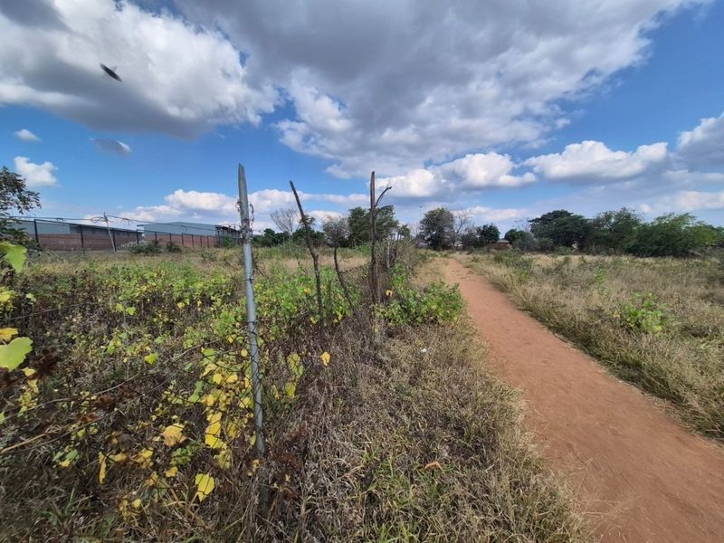 A view of a vacant residential plot featuring a dirt path and perimeter wire mesh fencing with some visible damage.