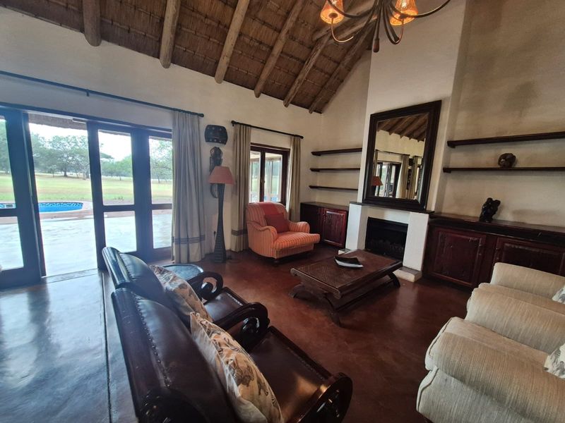 Spacious living room featuring a high thatched ceiling with exposed rafters, a fireplace, built-in cabinetry, and direct access to the outdoor patio area.