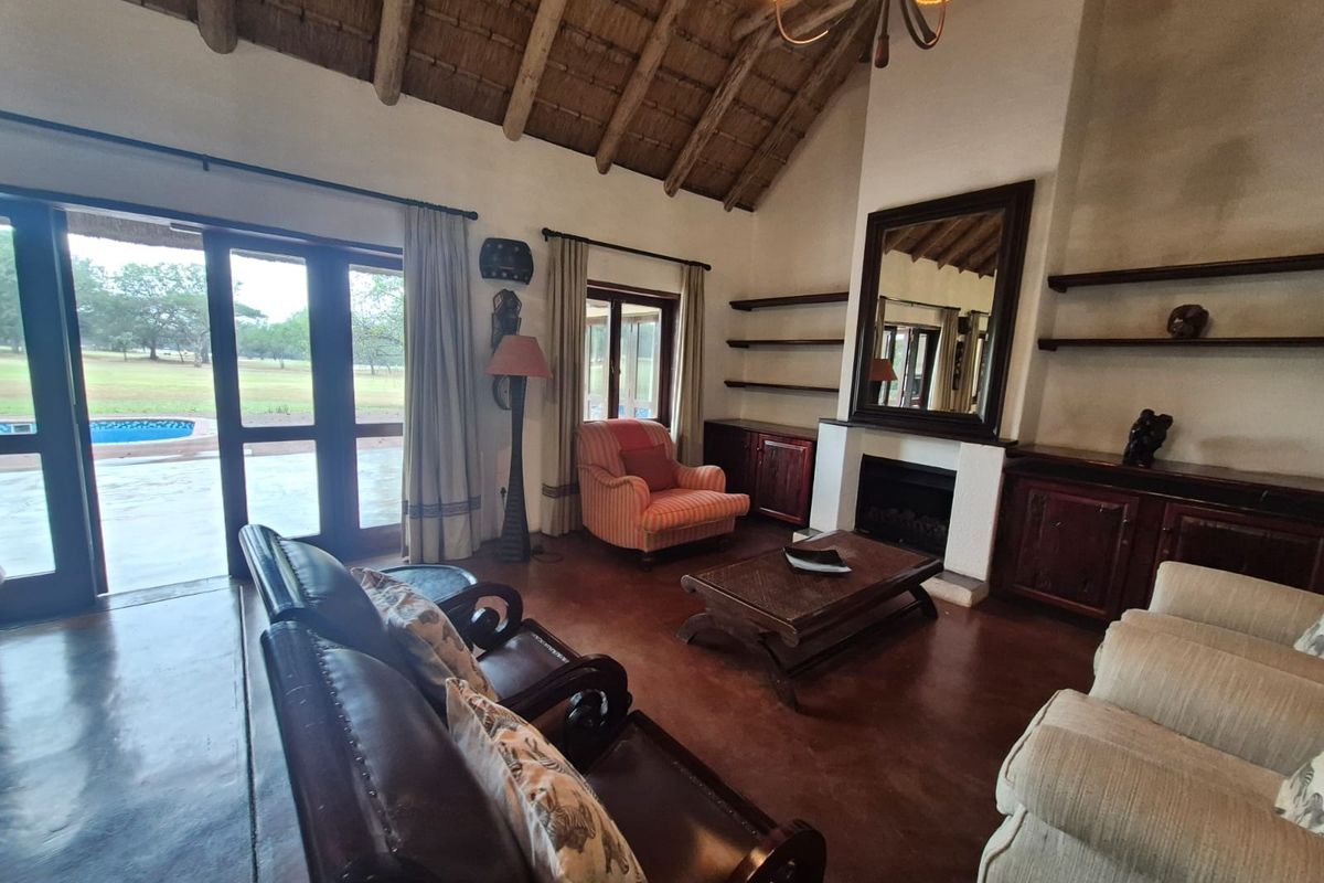 Spacious living room featuring a high thatched ceiling with exposed rafters, a fireplace, built-in cabinetry, and direct access to the outdoor patio area.