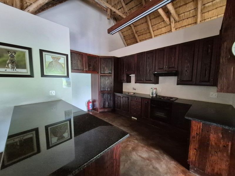 A rustic kitchen featuring dark wood cabinetry, granite countertops, built-in appliances, and a high-volume exposed thatch roof with timber rafters.