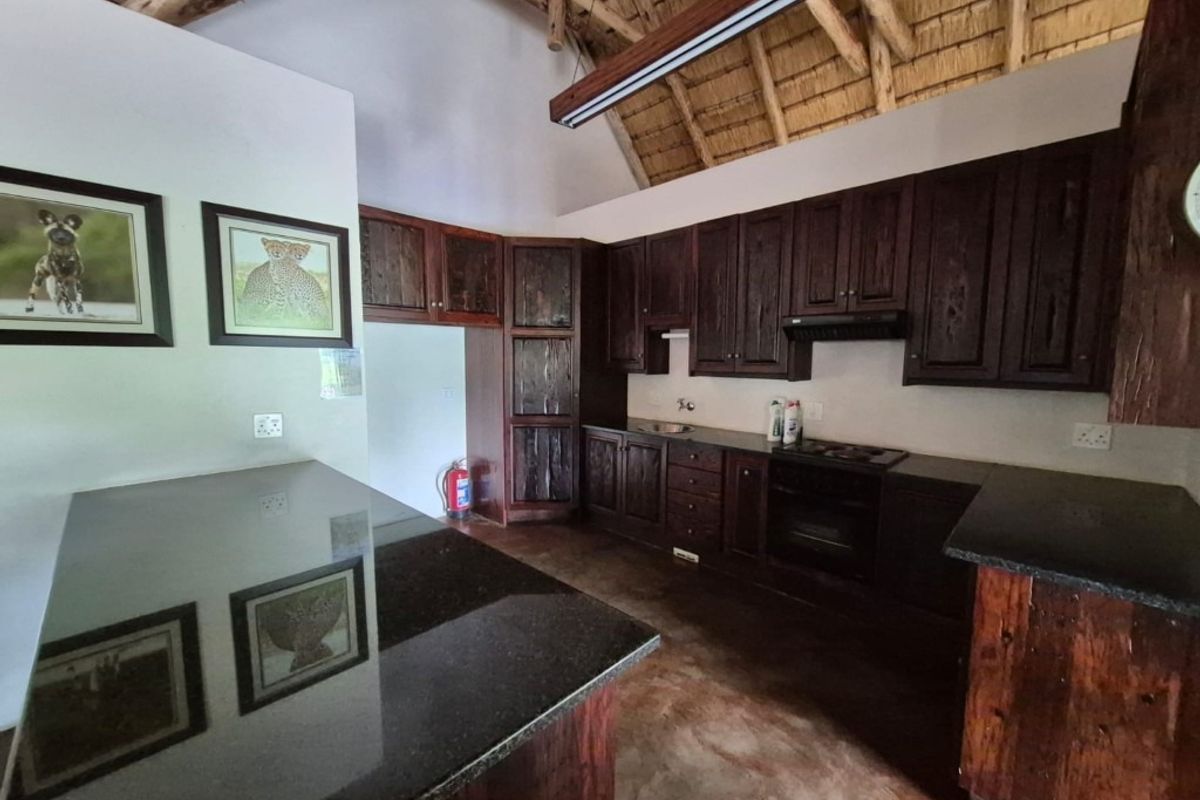 A rustic kitchen featuring dark wood cabinetry, granite countertops, built-in appliances, and a high-volume exposed thatch roof with timber rafters.