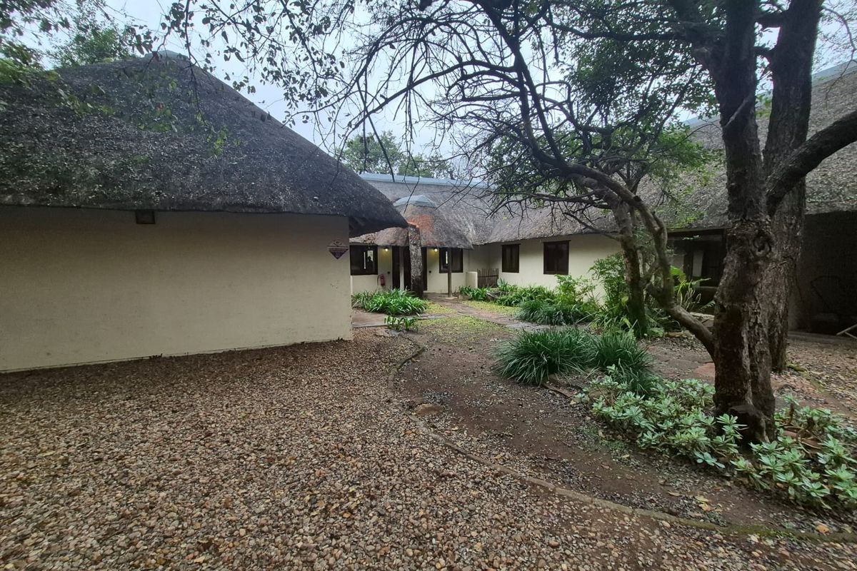A view of the rear exterior featuring traditional thatch roofing, a gravel courtyard area, and established garden landscaping with mature trees.