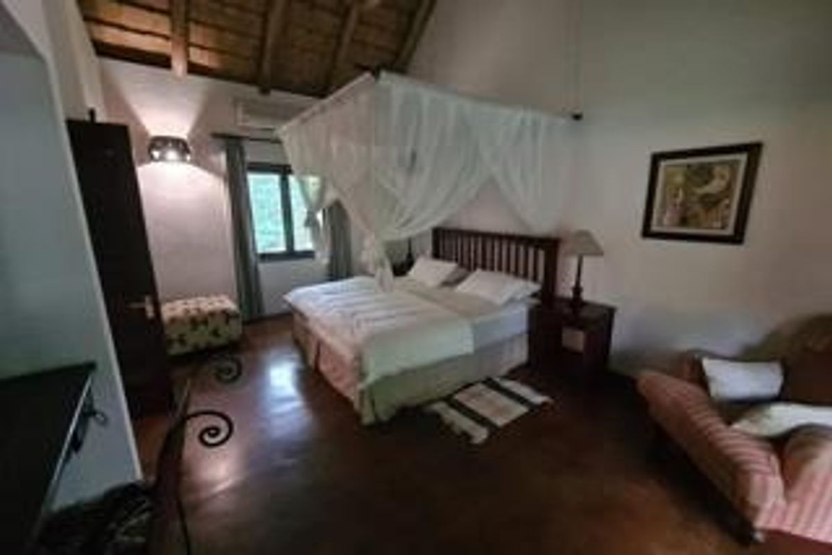 Spacious bedroom featuring high vaulted ceilings with exposed timber beams, tiled flooring, and a wall-mounted air conditioning unit.
