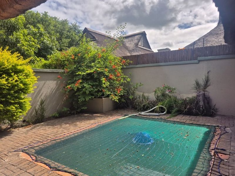 Outdoor pool area featuring a brick-paved surround, boundary wall, and a fitted pool safety net, set within a private garden space.