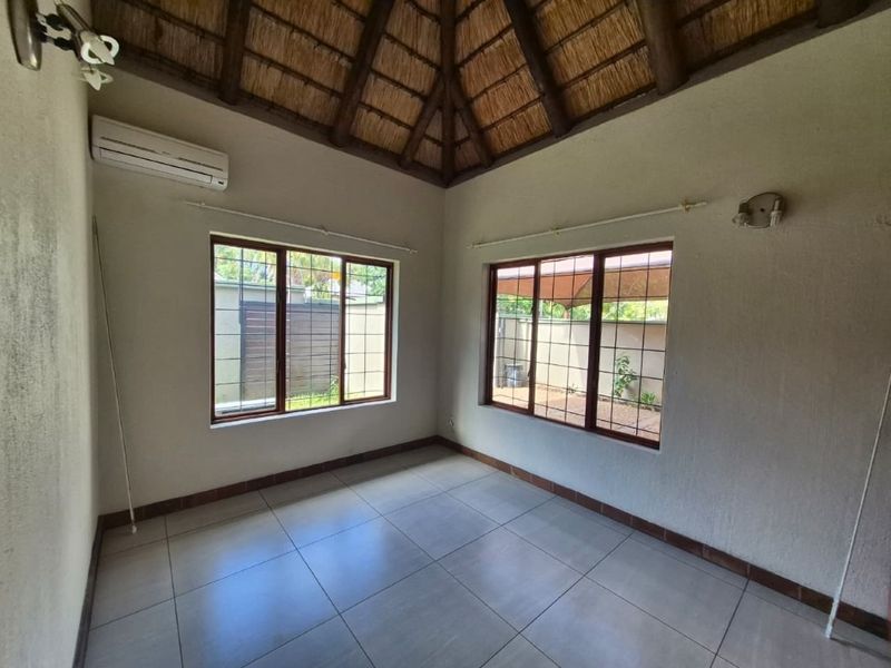 A bright, empty living room featuring a high thatched ceiling with exposed beams, tiled flooring, and split-system air conditioning.