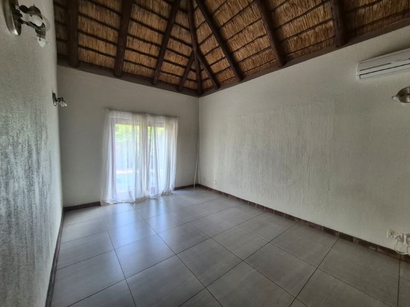 An empty bedroom featuring a high thatched ceiling with exposed timber beams, tiled flooring, and glass sliding doors leading to the exterior.