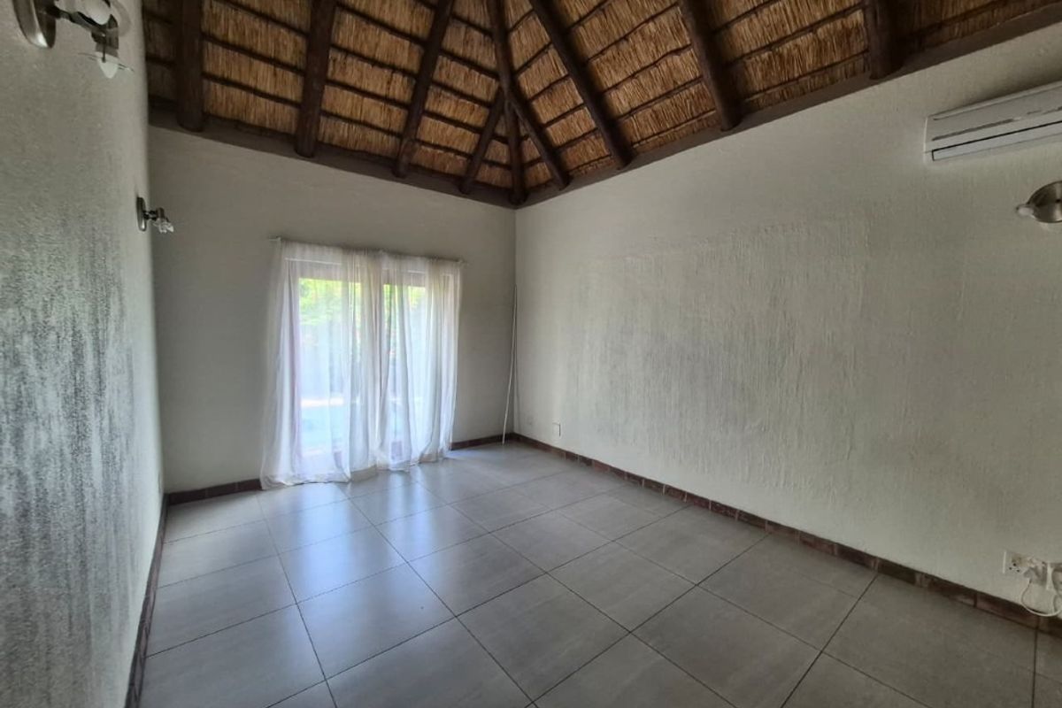 An empty bedroom featuring a high thatched ceiling with exposed timber beams, tiled flooring, and glass sliding doors leading to the exterior.