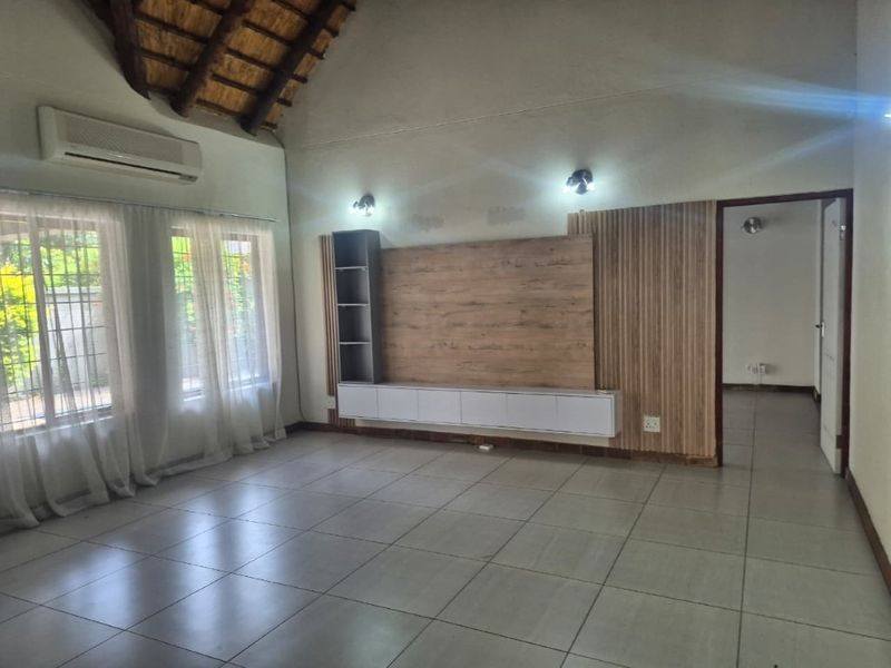 Spacious living room featuring a vaulted thatch ceiling, tiled flooring, split-system air conditioning, and a modern built-in media console with timber wall paneling.