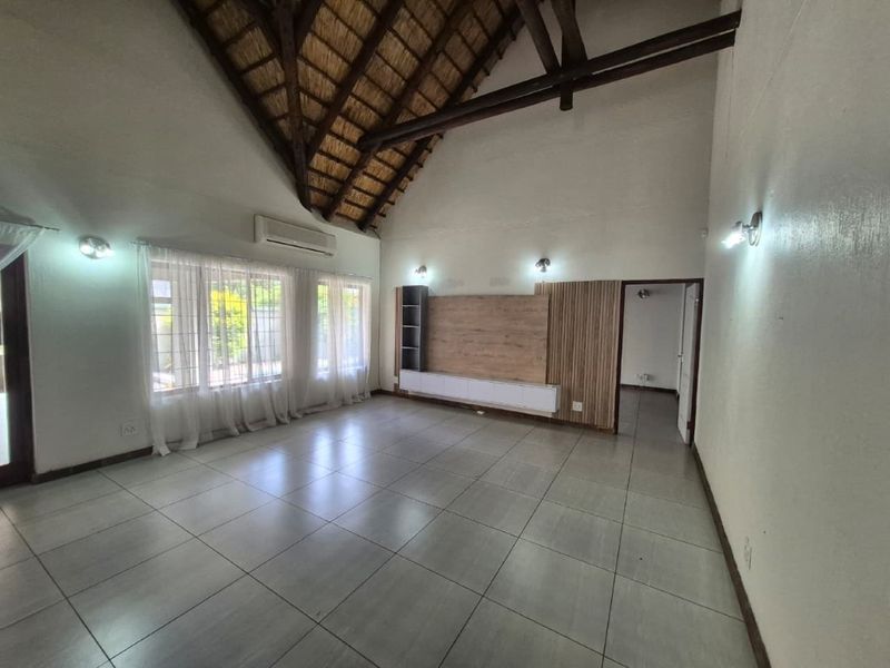 Spacious living area featuring a high vaulted thatched ceiling with exposed timber trusses, tiled flooring, and a built-in media console.