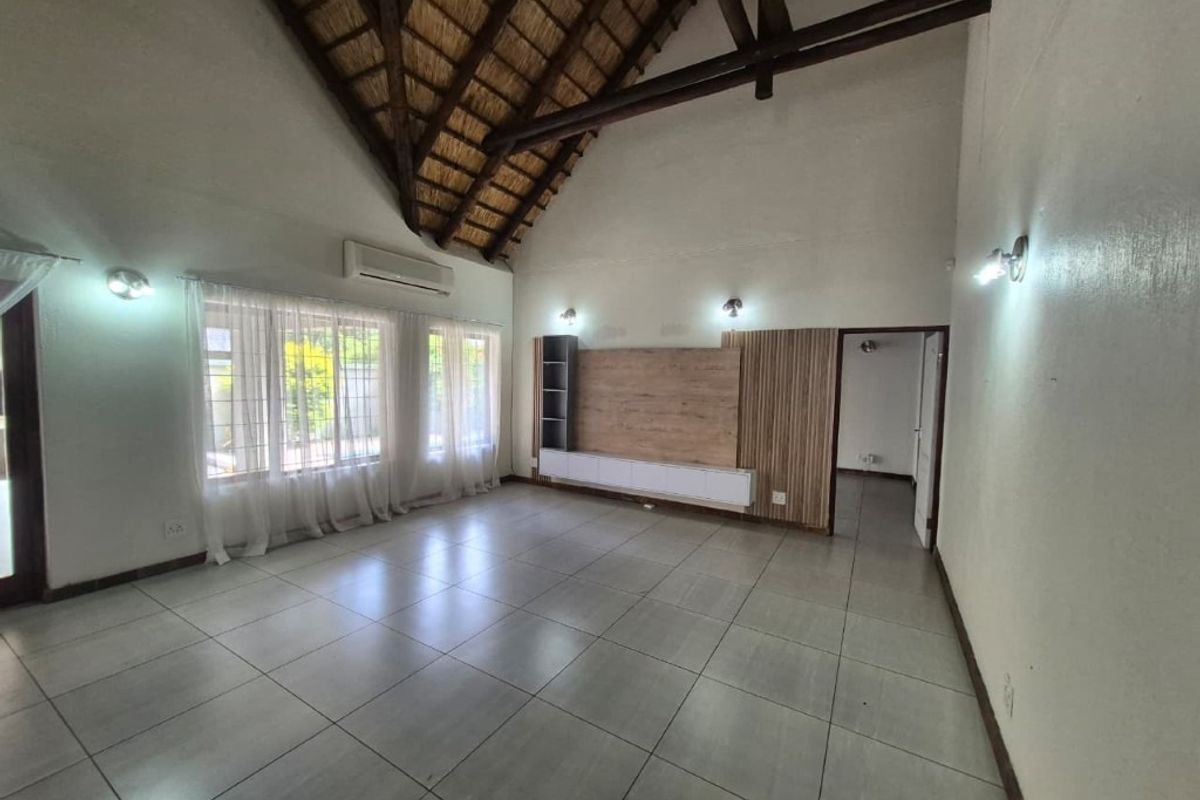 Spacious living area featuring a high vaulted thatched ceiling with exposed timber trusses, tiled flooring, and a built-in media console.