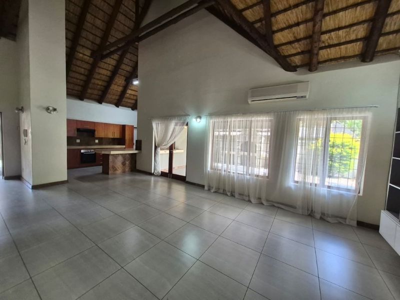 Spacious open-plan living area featuring high vaulted thatched ceilings with exposed timber trusses, tiled floors, and an integrated kitchen with built-in cabinetry.