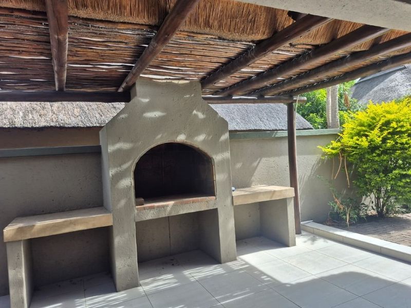 Outdoor patio area featuring a built-in braai with concrete prep surfaces and a traditional thatched roof covering.