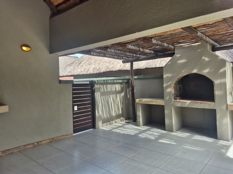 A covered outdoor patio featuring a built-in braai, tiled flooring, and a rustic thatched roof, providing an ideal space for outdoor entertaining.