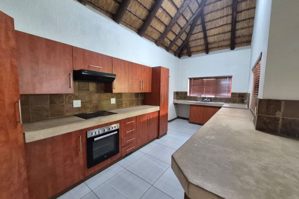 Spacious kitchen featuring wood-finish cabinetry, concrete countertops, built-in appliances, and a high vaulted thatched ceiling.