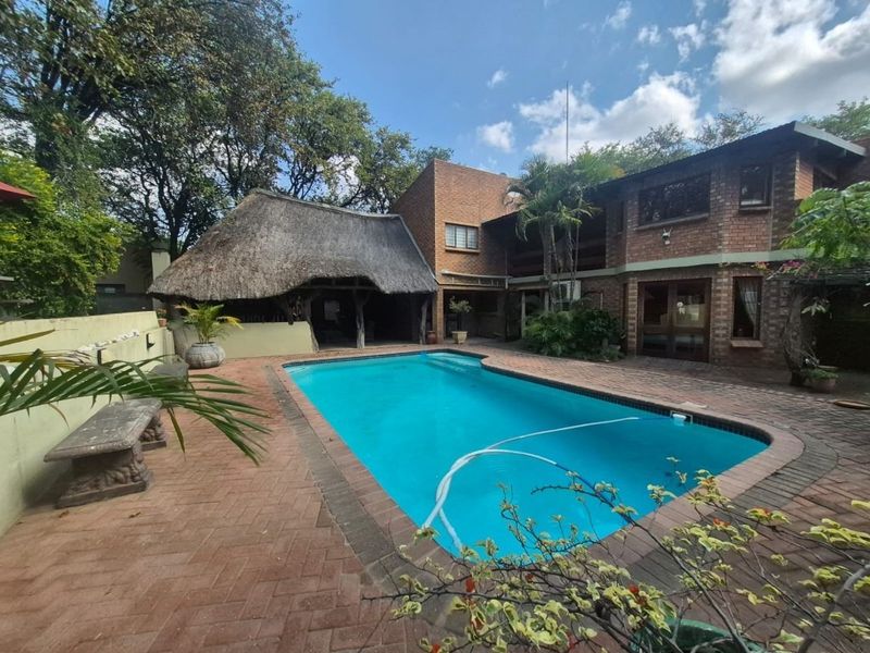 Outdoor pool area featuring a swimming pool, brick paved patio, and a traditional thatched lapa, set against a brick house exterior.