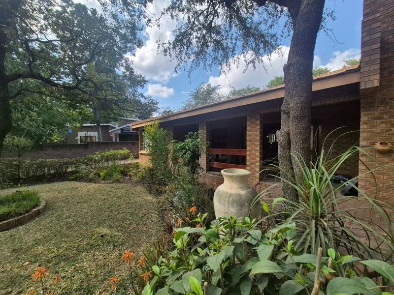 A view of the rear exterior featuring a covered brick patio, established garden, and mature trees.