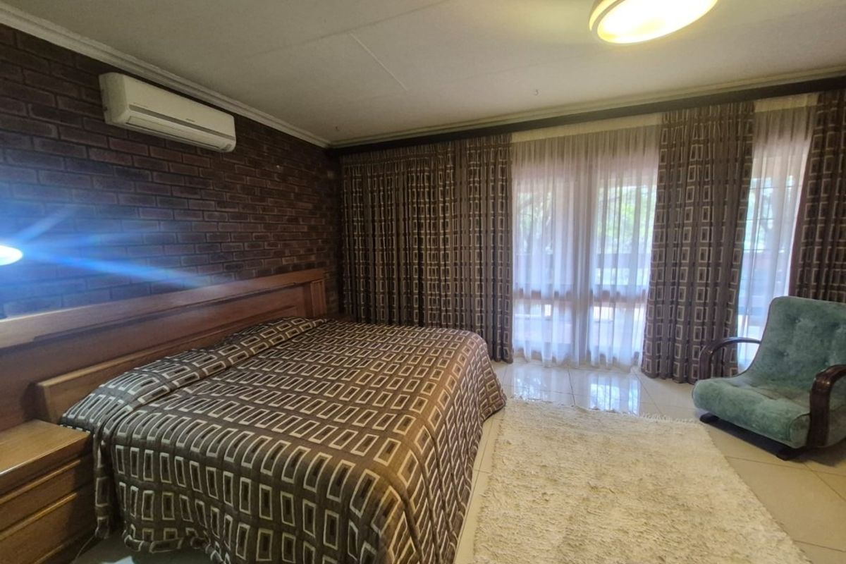 Spacious bedroom featuring an exposed brick feature wall, split-system air conditioning, and large sliding glass doors providing access to the exterior.