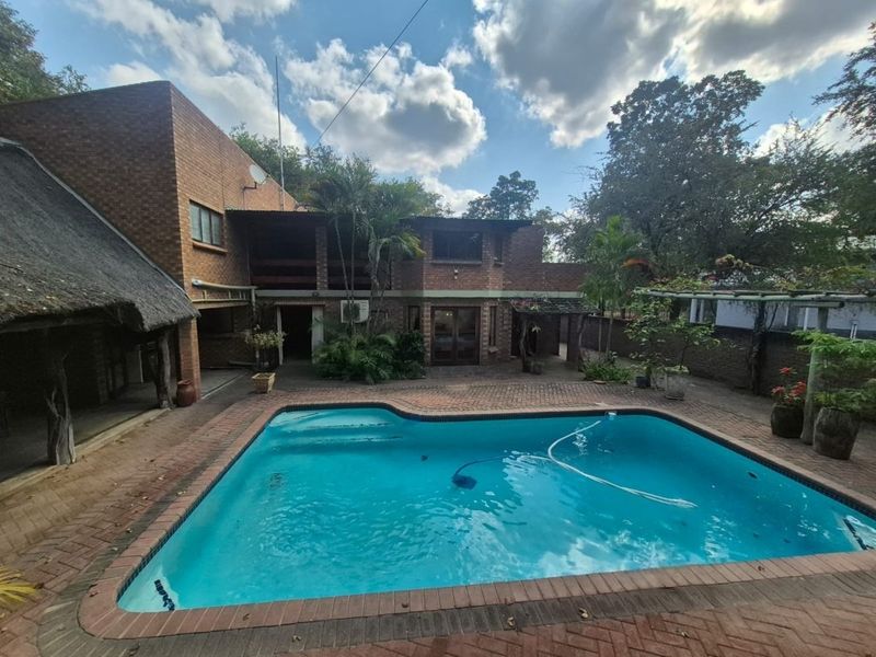 Rear exterior view featuring a swimming pool, brick paved patio area, and a combination of brick and thatched roof building structures.