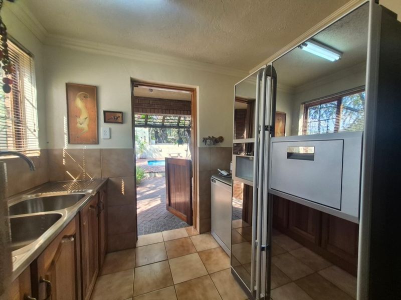 Functional scullery area featuring wooden cabinetry, double stainless steel sink, and tiled finishes, with direct access to the outdoor patio and pool area.