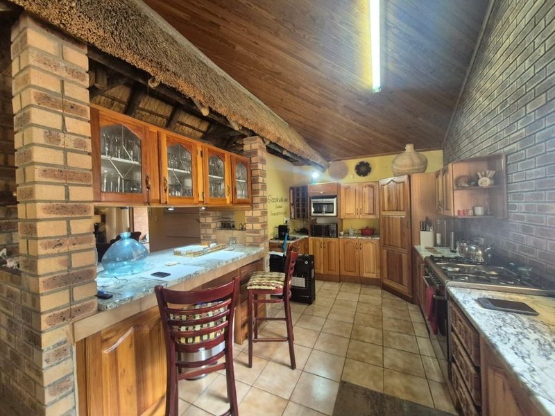 Spacious kitchen featuring timber cabinetry, granite countertops, built-in appliances, and a unique thatched ceiling with exposed brick walls.