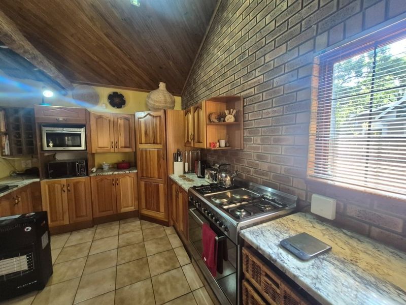 Rustic kitchen featuring wooden cabinetry, exposed brick walls, vaulted timber ceilings, and a gas stove with stone countertops.