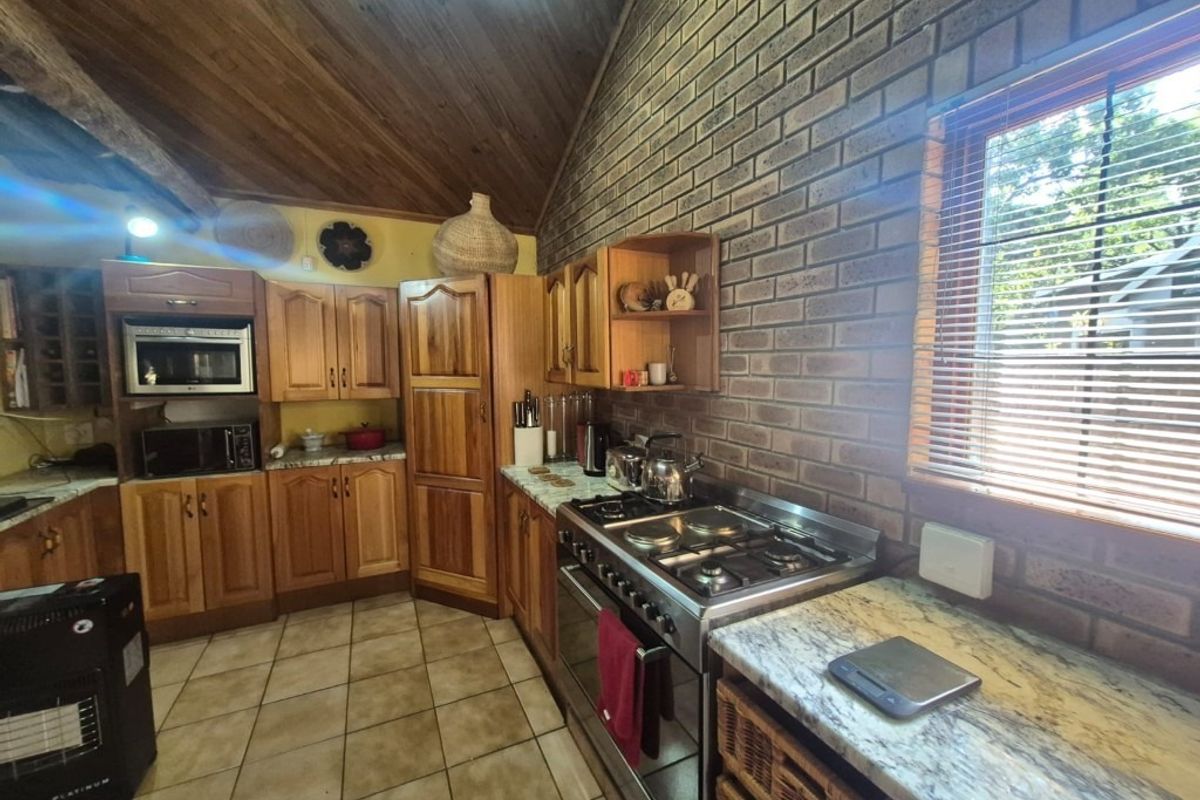 Rustic kitchen featuring wooden cabinetry, exposed brick walls, vaulted timber ceilings, and a gas stove with stone countertops.