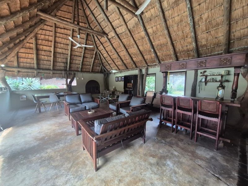 Spacious covered patio featuring a traditional thatched roof, exposed timber beams, a built-in bar, and a fireplace, ideal for outdoor entertaining.