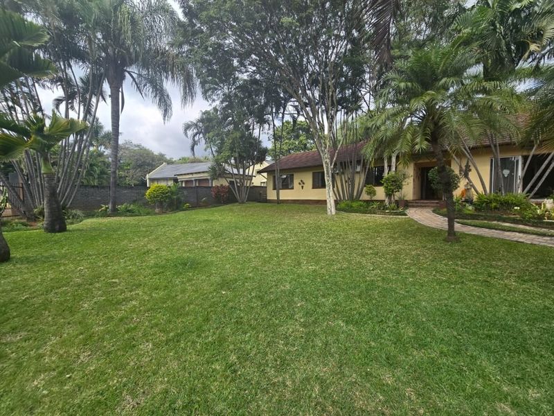 A spacious rear garden featuring a well-maintained lawn, mature trees, and a paved walkway leading to the main house structure.
