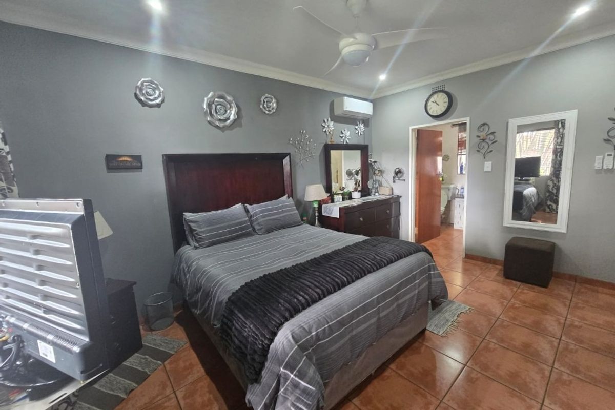 Spacious bedroom featuring tiled flooring, a ceiling fan, and a wall-mounted split-system air conditioner, with an adjoining en-suite bathroom.