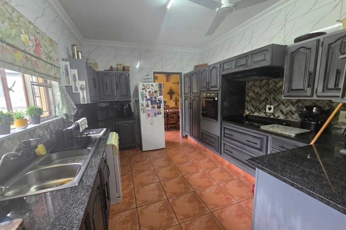 A functional kitchen featuring dark cabinetry, granite countertops, a double basin sink, built-in oven, and a herringbone tiled backsplash.